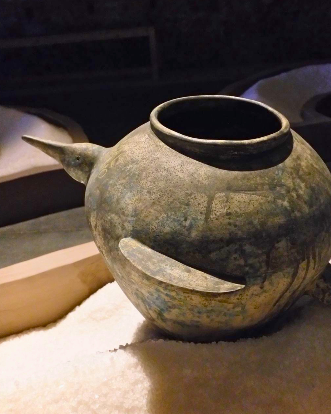 3 of 5, a ceramic vase with a beak like a bird, sits on salt within a platform on the ground